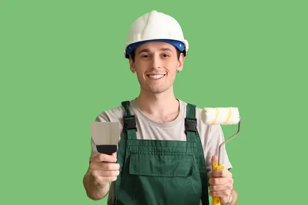 パティナイフと緑の背景にローラーを塗った男性労働者 — ストック写真