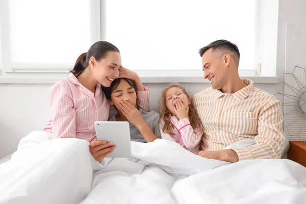 Sleepy little children with their parents using tablet computer in bedroom