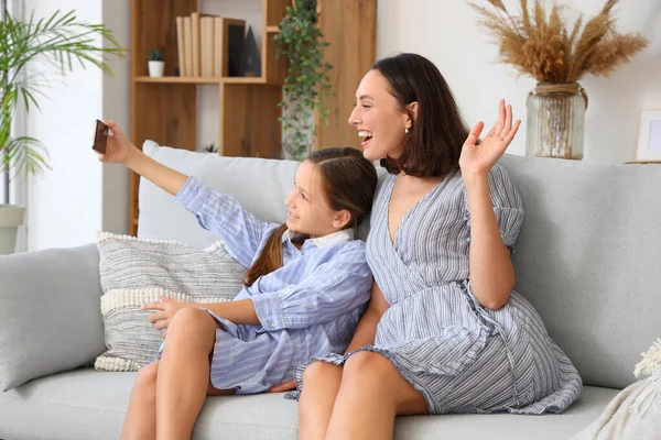 Mother and daughter talking selfie while sitting on grey sofa in living room