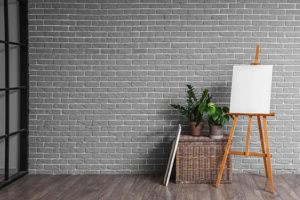 Wooden easel with blank canvas near grey brick wall