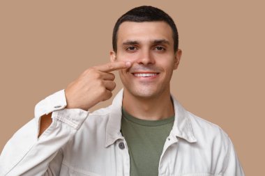 Genç adam kahverengi arka planda burnu işaret ediyor.