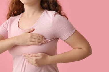 Pembe arka planda göğüslerini kontrol eden genç bir kadın, yakın plan. Kanser farkındalığı kavramı