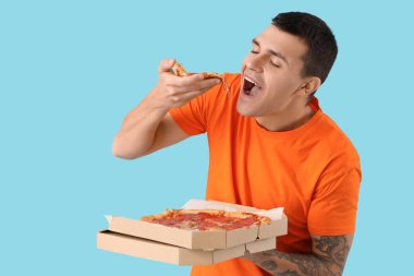 Mavi arka planda lezzetli biberli pizzalı genç adam.