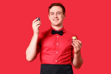 Genç erkek barmen, kırmızı arka planda tekila ve ölçü bardağıyla