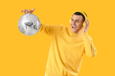 Sarı arka planda disko topu olan kulaklıklı genç bir adam.