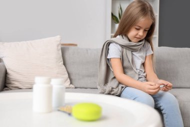 Evdeki kanepede oturan termometresi olan hasta küçük kız.