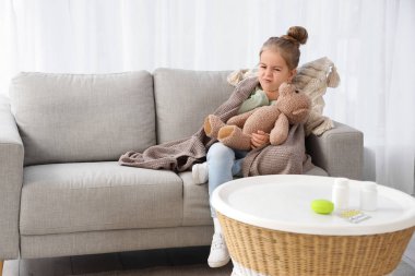 Hasta küçük kız ve oyuncak ayı evdeki kanepede oturuyor.