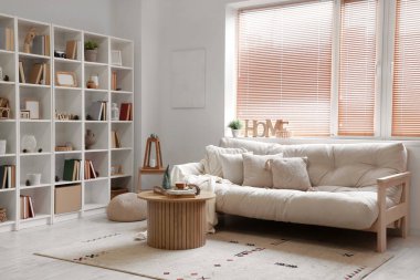 Konforlu kanepe, ahşap sehpa ve kitaplıklarla aydınlık oturma odasının içinde.