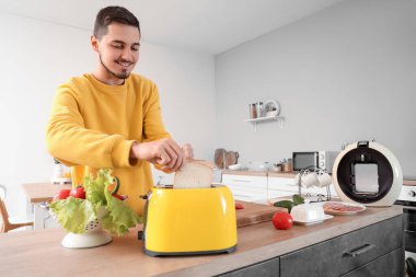 Genç adam mutfakta sandviçler için çıtır çıtır tost yapıyor.