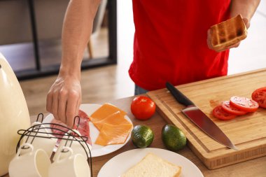 Genç adam lezzetli sandviçler yapıyor. Kızarmış ekmekler mutfakta, yakın plan.