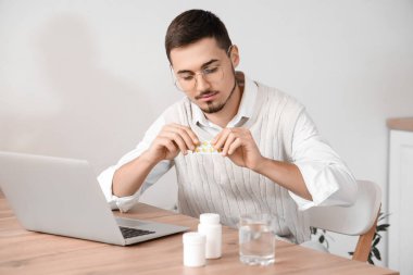 Bilgisayarlı genç adam evde hap alıyor.