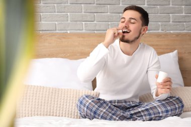 Genç adam yatak odasında uyumadan önce hap alıyor.