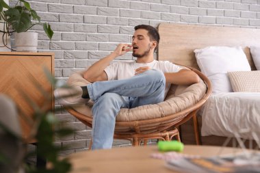 Genç adam oturma odasında hap alıyor.