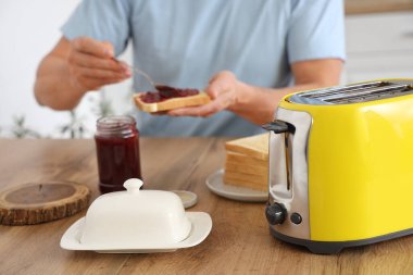 Orta yaşlı bir adam kahvaltıda tatlı reçelli ekmek yiyor, yakın plan.