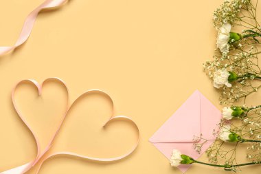 Çigila çiçekli beyaz karanfiller, sarı arka planda kalp şeklinde kurdeleler olan zarf. Sevgililer Günü konsepti