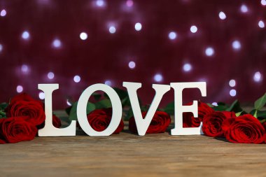 Red roses and word LOVE on wooden table