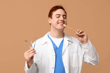 Male dentist with dental tools and toothbrush on beige background. World Dentist Day