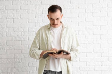 İncil 'i olan genç adam beyaz tuğla arka planda dua ediyor.