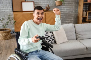 Evde video oyunu oynayan tekerlekli sandalyedeki mutlu genç adam.