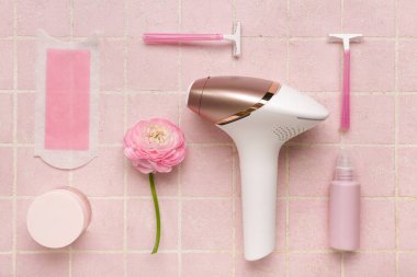 Balmumu şeritli modern fotoepilatör, jilet ve pembe fayanslı kozmetik ürünler.