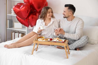 Sevgililer Günü 'nde yatakta kahvaltı yapan genç çift.