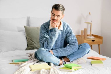 Yatak odasında kitapları olan düşünceli bir genç adam.