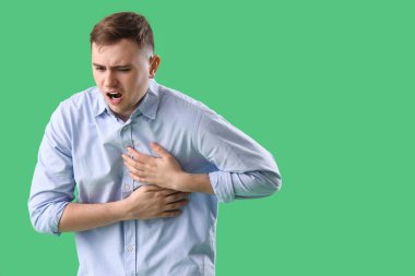 Yeşil arka planda göğüs ağrısı çeken genç bir adam.