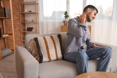 Evdeki kanepede boyun ağrısı çeken genç bir adam.