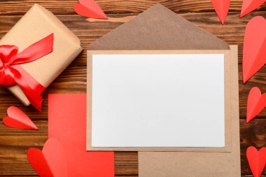 İçinde boş kart, hediye kutusu ve tahta arka planda kırmızı kağıt kalpler olan bir zarf. Sevgililer Günü kutlaması
