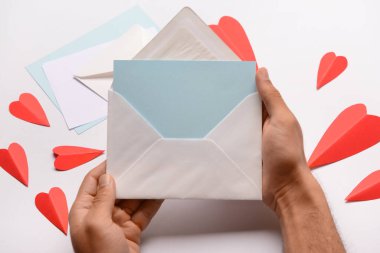 Zarflı erkek eller, boş kart ve beyaz arka planda kırmızı kağıt kalpler. Sevgililer Günü kutlaması