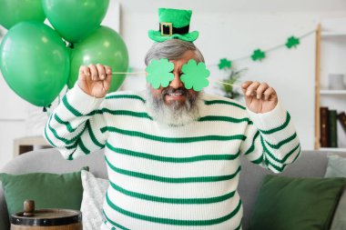 Aziz Patrick Günü 'nde evinde kağıt yoncalarla şapkalı olgun bir adam.