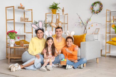 Paskalya yumurtaları evde yerde oturan tavşan kulaklı mutlu bir aile.