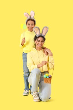 Küçük Afro-Amerikalı çocuk ve annesi, sarı arka planda Paskalya yumurtaları olan tavşan kulaklı.