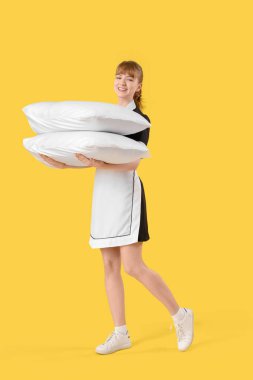 Sarı arka planda yastıkları olan genç oda hizmetçisi