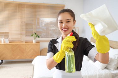 Yatak odasında deterjanı ve bezi olan genç Asyalı oda hizmetçisi.