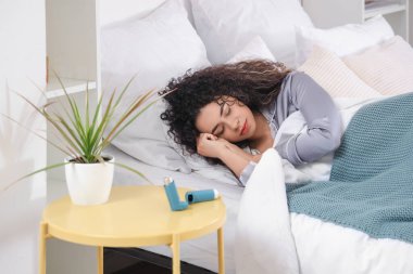Yatak odasındaki astım spreyli uyuyan Afro-Amerikalı kadın.