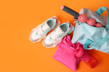 Spor giyimli spor çantası, ayakkabılar, su şişesi ve turuncu arka planda spor malzemeleri.