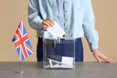 Oy kullanma merkezindeki oy sandığının yanında İngiliz bayrağı taşıyan genç bir kadın.