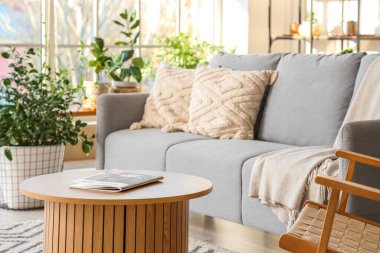 Rahat kanepesi, koltuğu, çiçekleri ve masası olan modern bir oturma odası.