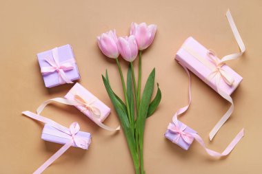 Bej arka planda hediye kutuları ve pembe laleler olan kompozisyon. Üst görünüm