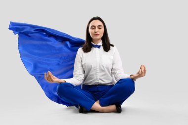 Süper kahraman pelerinli iş kadını hafif arka planda meditasyon yapıyor.