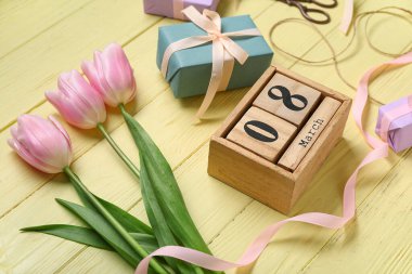 8 Mart tarihli küp takvimi, hediye kutuları, pembe laleler ve sarı ahşap arka planda makas. Uluslararası Kadınlar Günü kutlamaları