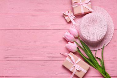 Hediye kutuları, pembe laleler ve pembe ahşap masada hasır şapka. Üst görünüm