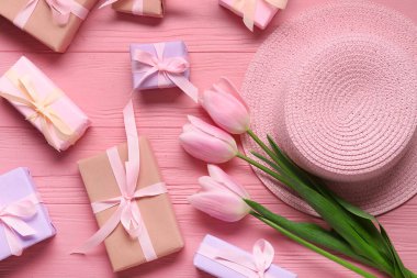 Hediye kutuları, pembe laleler ve pembe ahşap masada hasır şapka. Üst görünüm