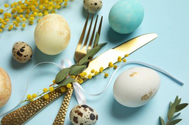 Masa takımı için çatal bıçak takımı ve mavi arka planda Paskalya yumurtası.
