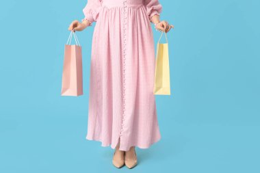 Mavi arka planda alışveriş torbaları olan zarif pembe elbiseli genç bir kadın.