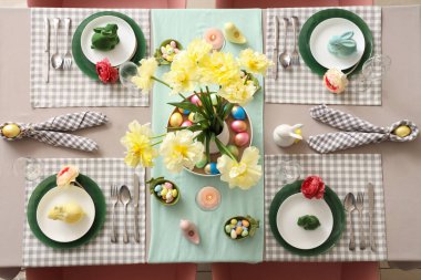 Paskalya sofrasında vazolar dolusu çiçek, peçeteler, boyanmış yumurtalar ve paskalya tavşanları.