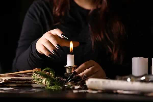 Witch with burning candle at dark table, closeup