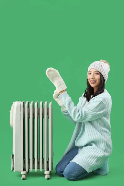 緑の背景にラジエーターと冬の服の若いアジアの女性 — ストック写真