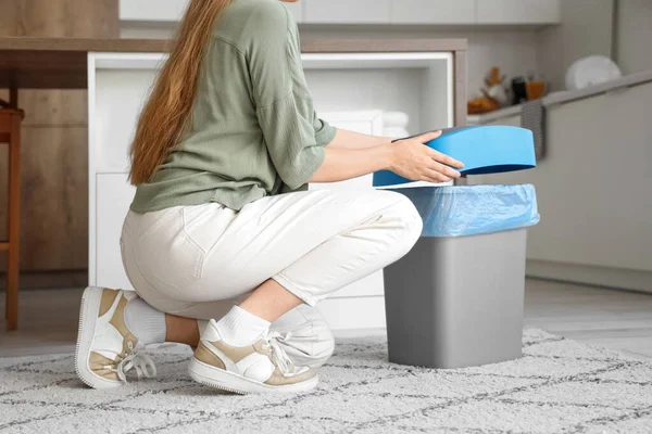 Woman closing lid of empty trash bin in kitchen
